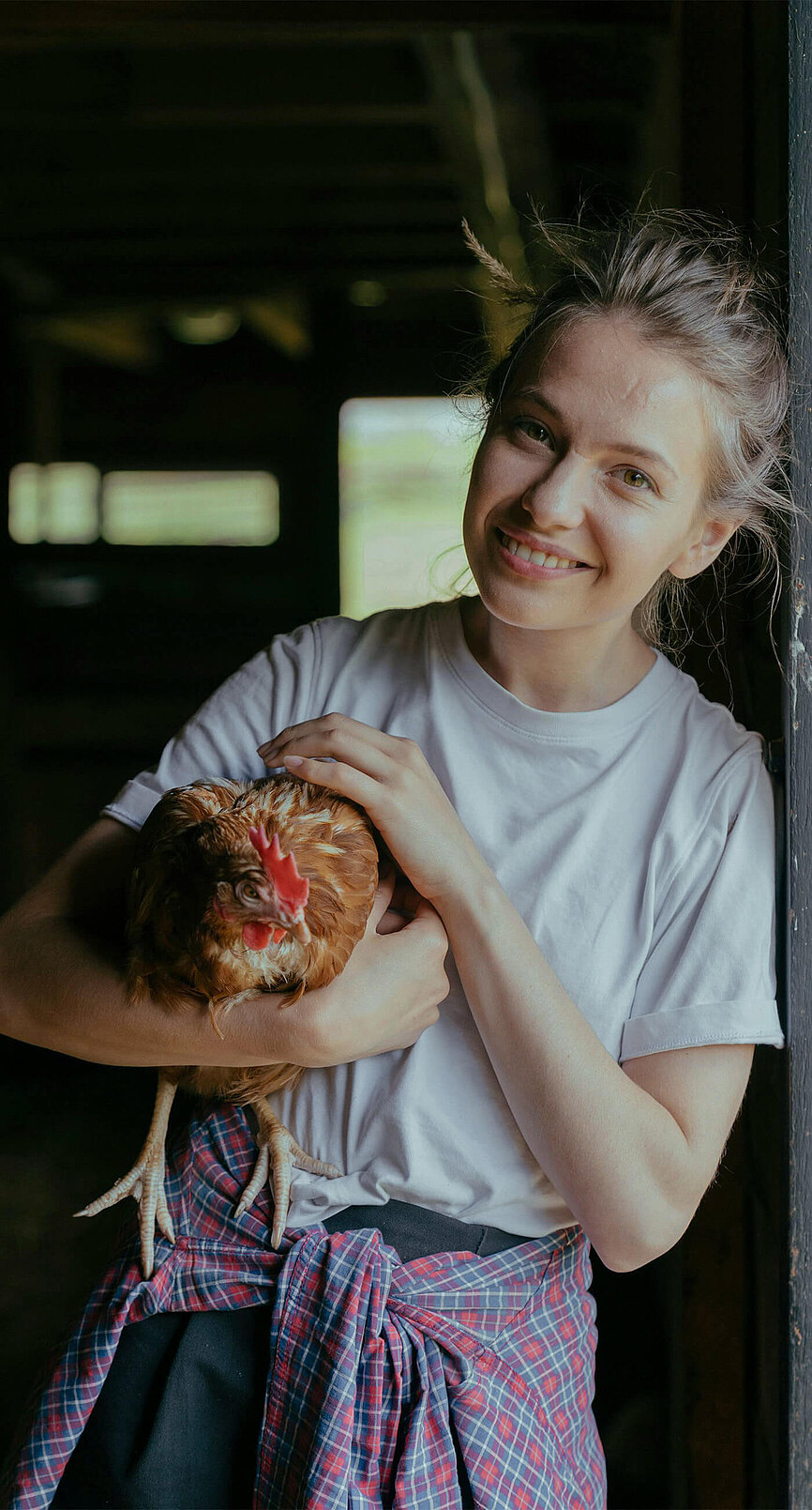 Eine Frau streichelt lächelnd das Huhn in ihrem Arm und möchte ihr Vermögen nachhaltig anlegen.